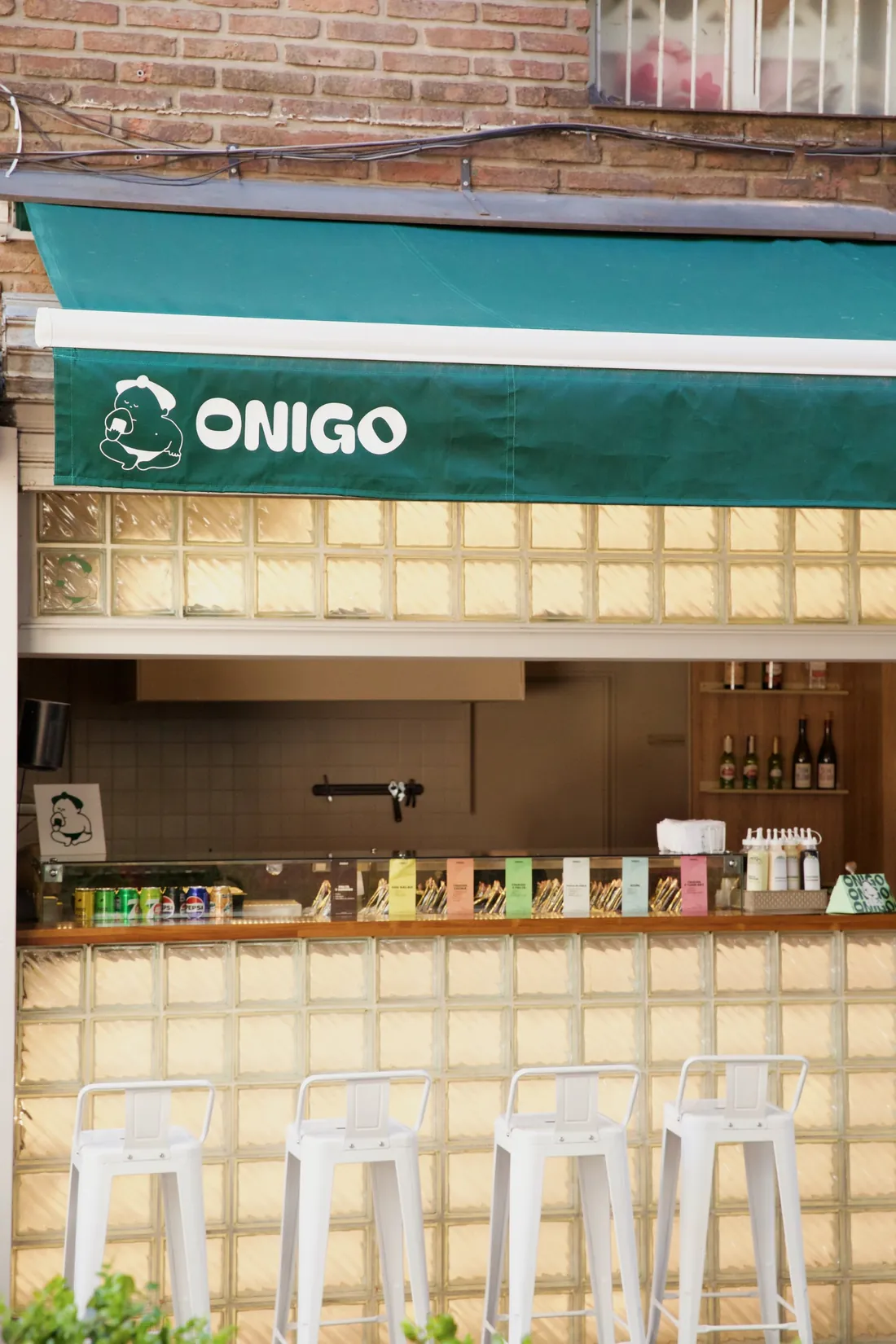 El local de Onigo: toldo verde con el logo, barra de bloques de vidrio y banquetas blancas