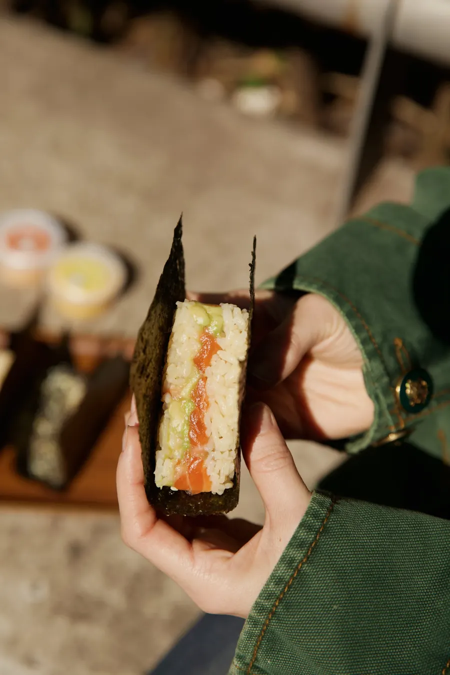 Onigo de salmón y palta abierto, sostenido con la mano